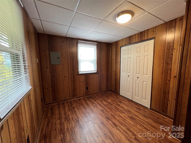 unfurnished bedroom with dark wood-type flooring, a paneled ceiling, wooden walls, and a closet