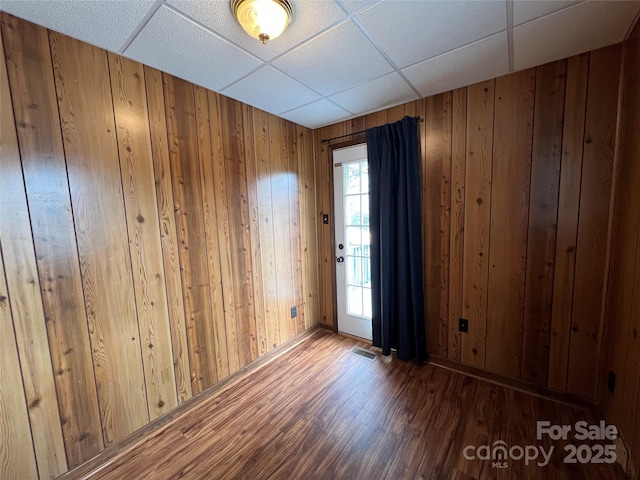 spare room featuring dark wood-type flooring, wood walls, and a drop ceiling