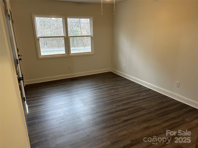 spare room with dark wood-style flooring, visible vents, and baseboards