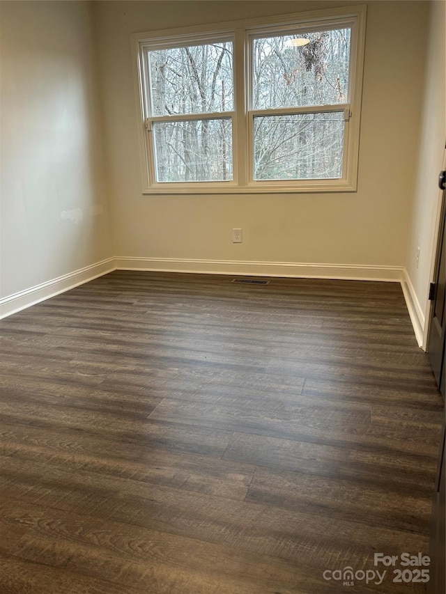 empty room with visible vents, dark wood finished floors, and baseboards