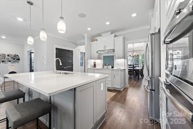 kitchen featuring sink, white cabinetry, decorative light fixtures, appliances with stainless steel finishes, and a kitchen island with sink