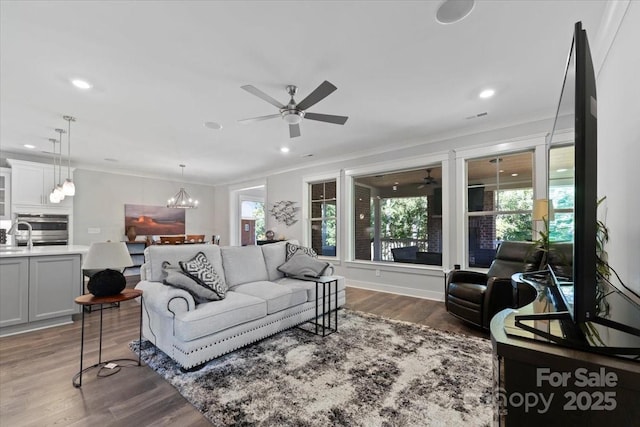 living room featuring crown molding, a wealth of natural light, dark hardwood / wood-style floors, and ceiling fan with notable chandelier