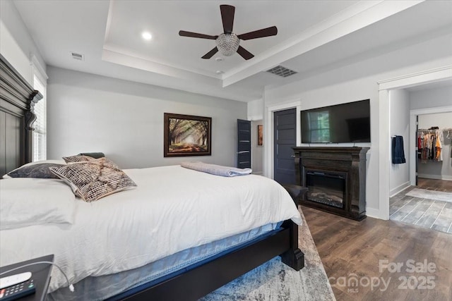 bedroom featuring a raised ceiling, dark hardwood / wood-style floors, ceiling fan, and a spacious closet