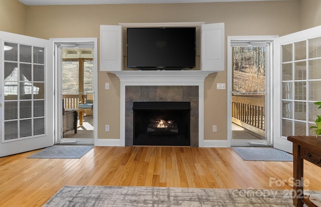 unfurnished living room featuring a tile fireplace, wood-type flooring, and baseboards