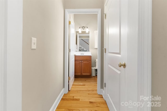 corridor featuring light wood-style floors, baseboards, and a sink