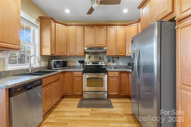 kitchen with light wood-type flooring, under cabinet range hood, stainless steel appliances, and a sink