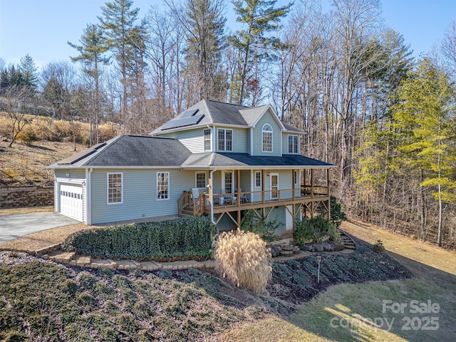 view of front facade featuring a shingled roof, concrete driveway, an attached garage, covered porch, and roof mounted solar panels