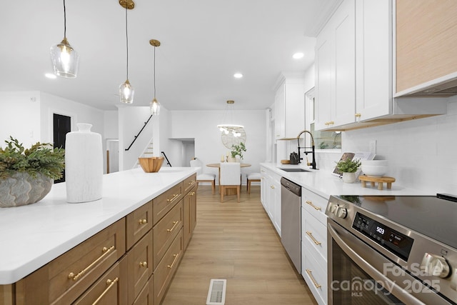 kitchen featuring sink, white cabinets, hanging light fixtures, stainless steel appliances, and light wood-type flooring