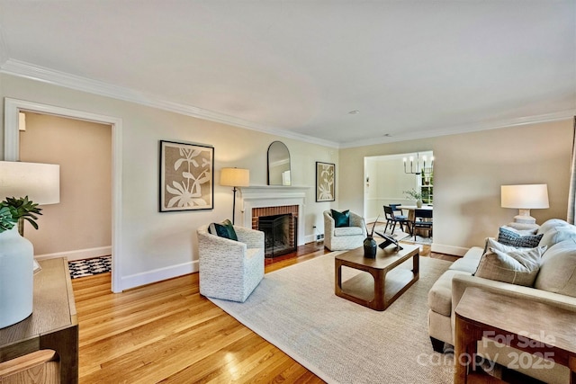 living room featuring crown molding, a fireplace, a chandelier, and light hardwood / wood-style flooring