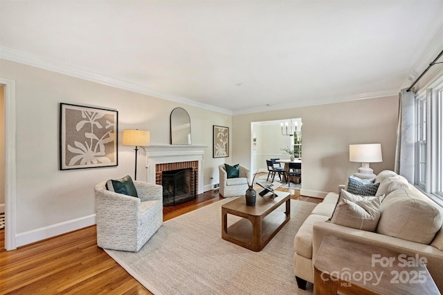 living room featuring an inviting chandelier, a brick fireplace, light hardwood / wood-style flooring, and ornamental molding