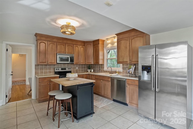 kitchen featuring sink, a center island, light tile patterned floors, stainless steel appliances, and backsplash