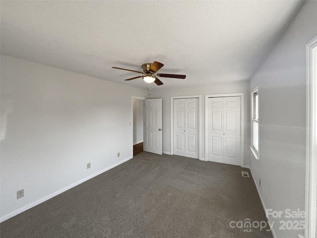 unfurnished bedroom featuring multiple closets, dark colored carpet, ceiling fan, and a textured ceiling