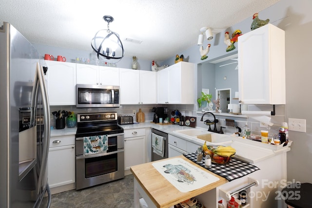 kitchen featuring sink, appliances with stainless steel finishes, hanging light fixtures, white cabinets, and decorative backsplash