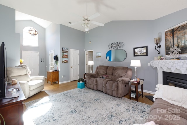 living room featuring high vaulted ceiling, light hardwood / wood-style floors, a premium fireplace, and ceiling fan