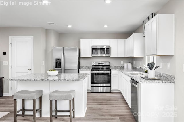 kitchen with stainless steel appliances, white cabinetry, a kitchen island, and light stone countertops