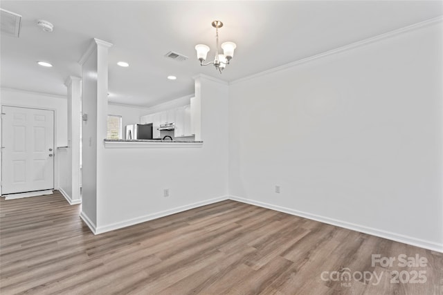 unfurnished dining area with an inviting chandelier, ornamental molding, and light hardwood / wood-style floors