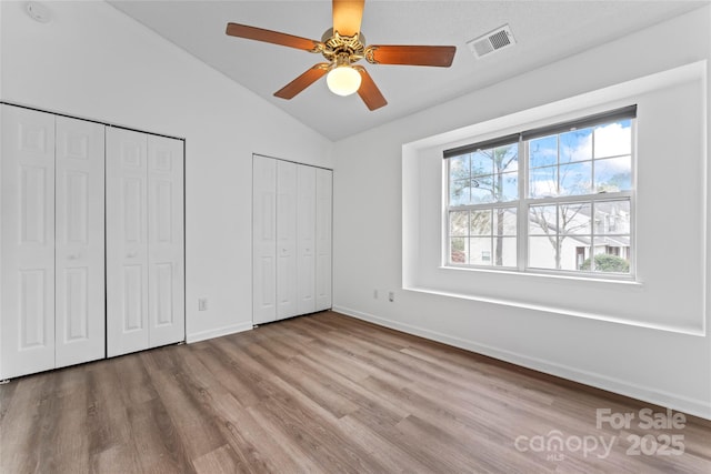 unfurnished bedroom with multiple closets, ceiling fan, vaulted ceiling, and light wood-type flooring