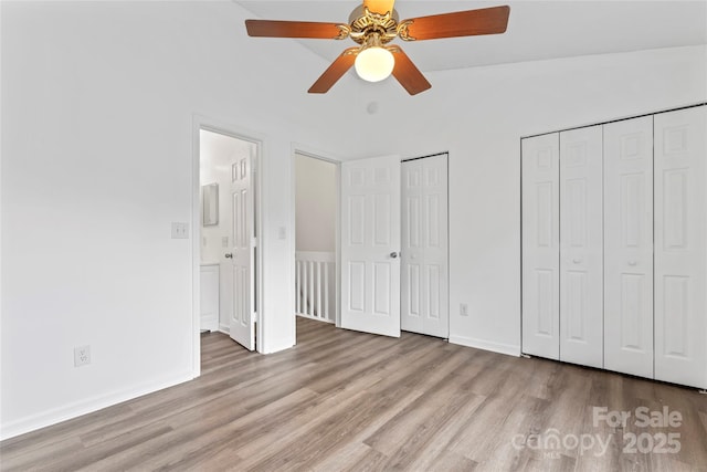 unfurnished bedroom with vaulted ceiling, connected bathroom, ceiling fan, multiple closets, and light wood-type flooring