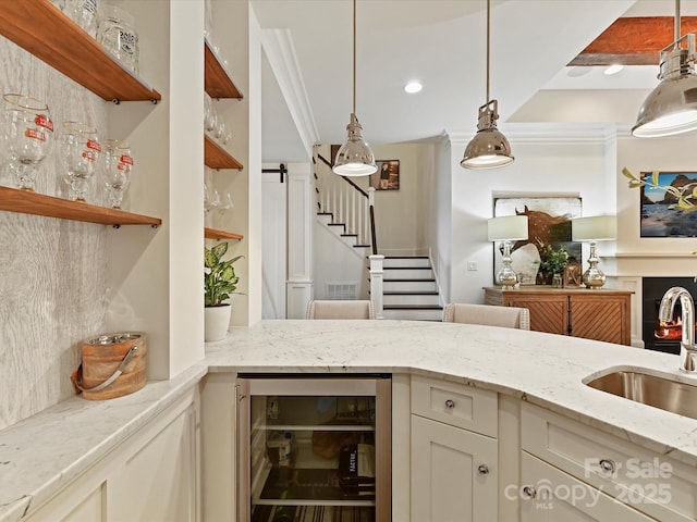 interior space with sink, crown molding, light stone countertops, decorative light fixtures, and beverage cooler