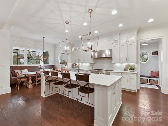 kitchen featuring hanging light fixtures, sink, white cabinets, and a center island with sink