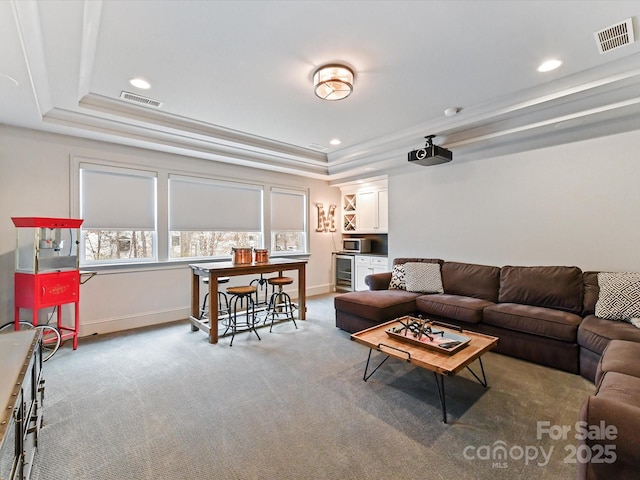 living room with wine cooler, light colored carpet, ornamental molding, and a tray ceiling