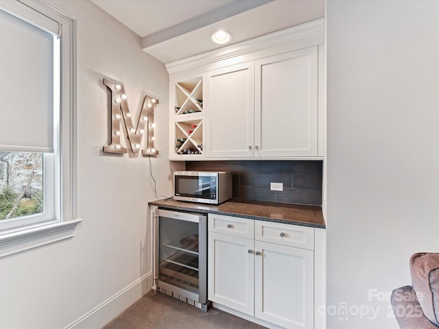 bar with white cabinetry, wine cooler, decorative backsplash, light colored carpet, and dark stone counters