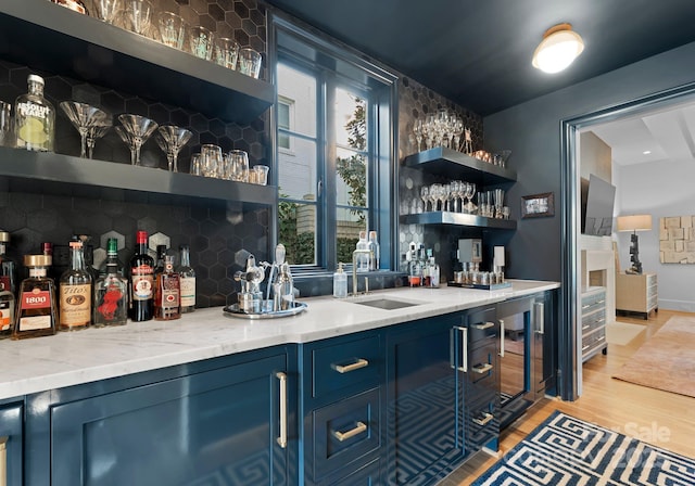 bar featuring blue cabinets, sink, light wood-type flooring, light stone countertops, and decorative backsplash