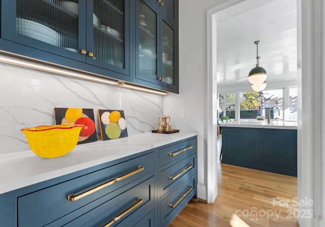 bar featuring blue cabinets, pendant lighting, backsplash, and light hardwood / wood-style floors