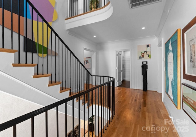 stairway with ornamental molding and hardwood / wood-style floors