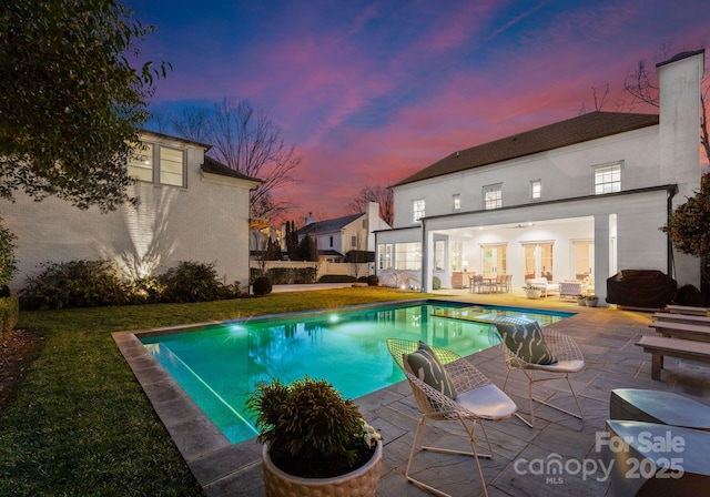 pool at dusk featuring a patio and a lawn