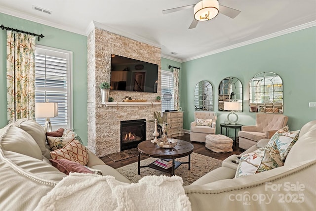 living room with hardwood / wood-style flooring, crown molding, a stone fireplace, and ceiling fan