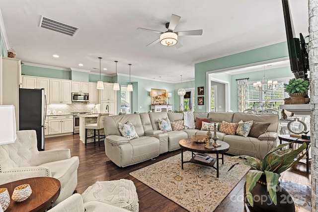 living room with crown molding, dark wood-type flooring, a wealth of natural light, and ceiling fan with notable chandelier