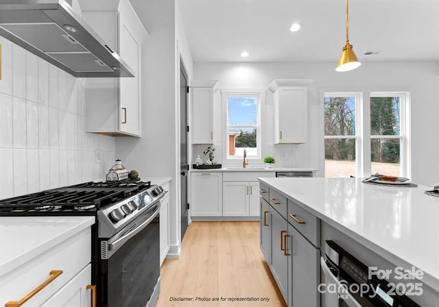 kitchen with wall chimney exhaust hood, pendant lighting, stainless steel range with gas cooktop, and white cabinets