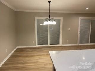 unfurnished dining area featuring crown molding, hardwood / wood-style floors, and a notable chandelier