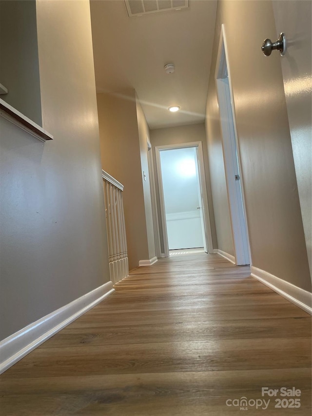 hall featuring wood finished floors, visible vents, and baseboards