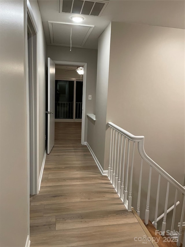 hall with wood finished floors, visible vents, baseboards, attic access, and an upstairs landing