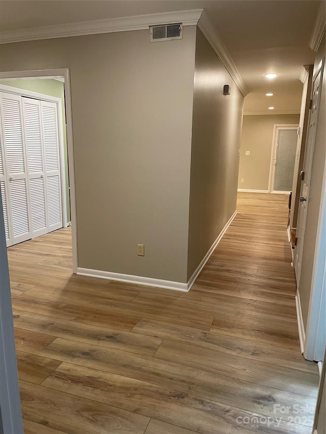 hallway featuring baseboards, wood finished floors, visible vents, and ornamental molding