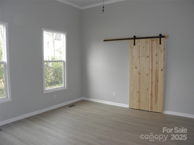 unfurnished room with ornamental molding, a barn door, and light hardwood / wood-style floors