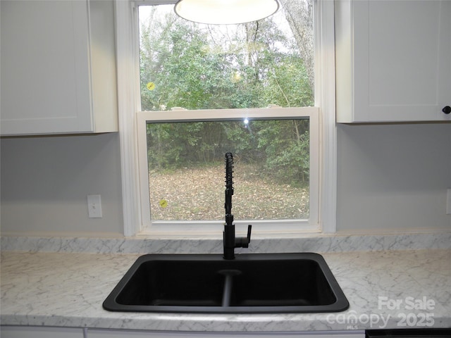 kitchen featuring light stone counters, sink, a healthy amount of sunlight, and white cabinets