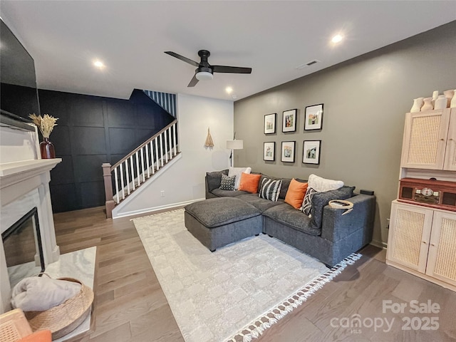 living room featuring a premium fireplace, ceiling fan, and light wood-type flooring