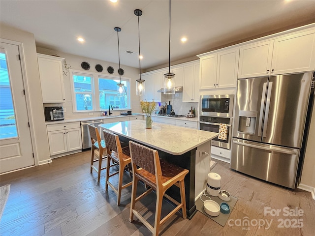 kitchen with a kitchen island, appliances with stainless steel finishes, a breakfast bar, sink, and white cabinets