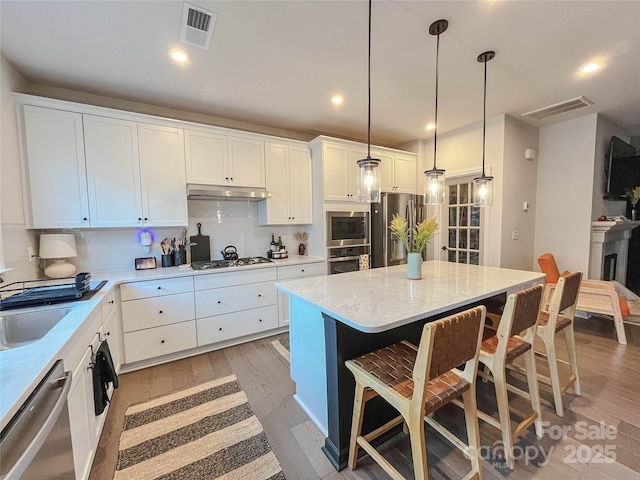 kitchen featuring white cabinetry, stainless steel appliances, decorative light fixtures, and a kitchen island