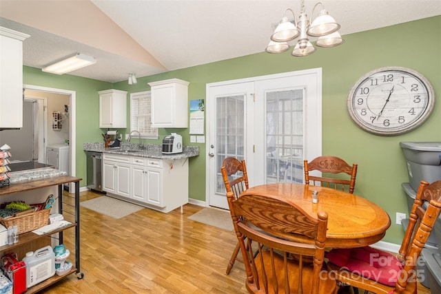 dining space featuring vaulted ceiling, washer / dryer, sink, a notable chandelier, and light hardwood / wood-style flooring