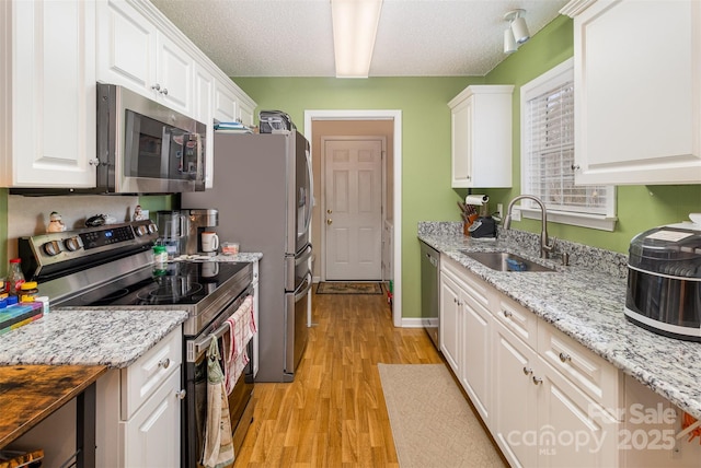 kitchen with white cabinetry, appliances with stainless steel finishes, light stone countertops, and sink