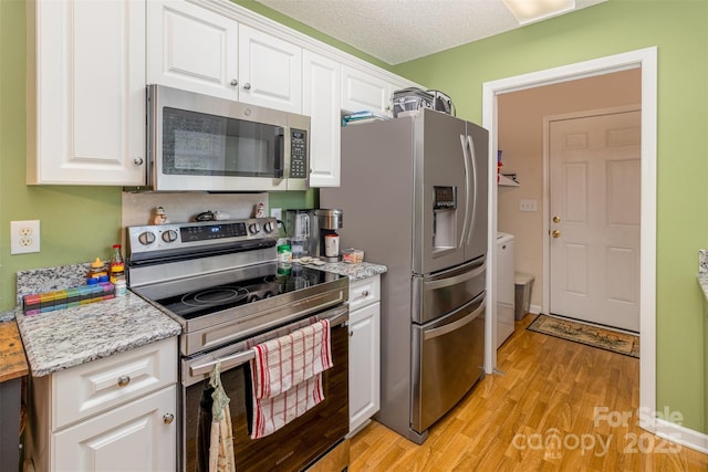 kitchen with stainless steel appliances, white cabinetry, washer and dryer, and light hardwood / wood-style floors