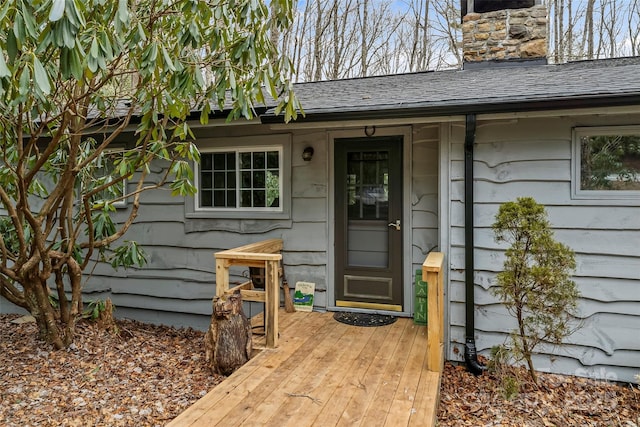 entrance to property featuring a shingled roof and a chimney