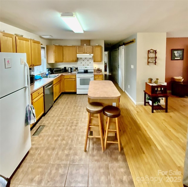 kitchen featuring sink, light tile patterned floors, a kitchen breakfast bar, white appliances, and a barn door