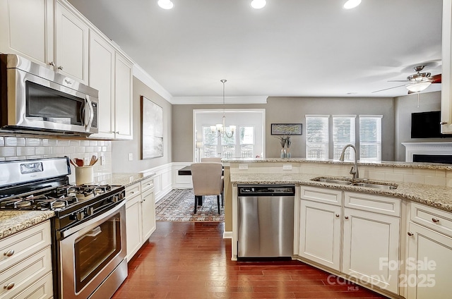 kitchen with appliances with stainless steel finishes, dark hardwood / wood-style floors, decorative light fixtures, sink, and light stone counters