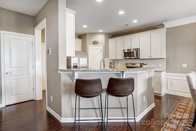 kitchen featuring appliances with stainless steel finishes, dark hardwood / wood-style flooring, light stone countertops, and white cabinets