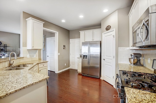 kitchen with appliances with stainless steel finishes, dark hardwood / wood-style floors, white cabinetry, sink, and light stone counters